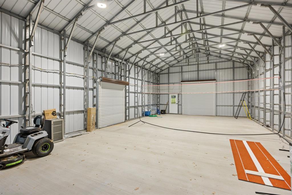 1800 Knox Road Tolar, TX 76476 - Photo 35 of 38 Spacious metal building featuring a vaulted truss ceiling, corrugated metal walls, concrete flooring, and multiple overhead light fixtures.