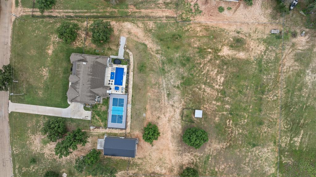 1800 Knox Road Tolar, TX 76476 - Photo 36 of 38 Expansive grounds featuring a multi-gabled residence, a structured swimming pool, an adjacent paved sports court, a separate barn-style outbuilding, and mature trees dotting the landscape