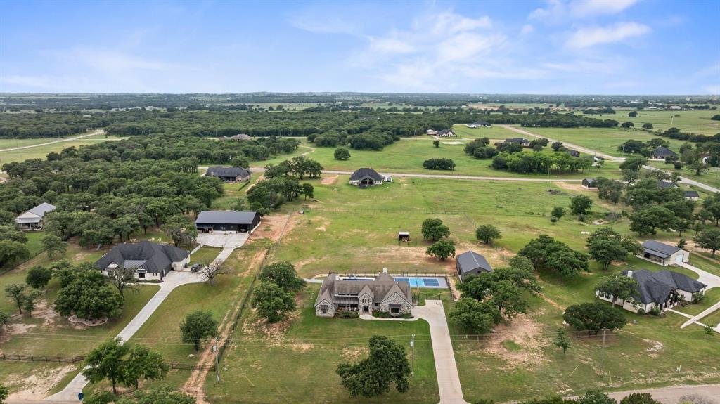 1800 Knox Road Tolar, TX 76476 - Photo 37 of 38 Expansive property featuring a stone exterior residence with a rectangular swimming pool, accompanied by a detached outbuilding and concrete driveway