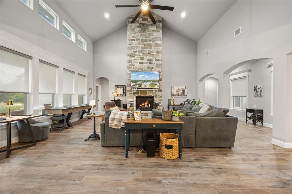 1800 Knox Road Tolar, TX 76476 - Photo 7 of 38 Expansive living area featuring vaulted ceilings, a stone-clad fireplace with a hearth, wood-finish flooring, and multiple large windows with roller shades