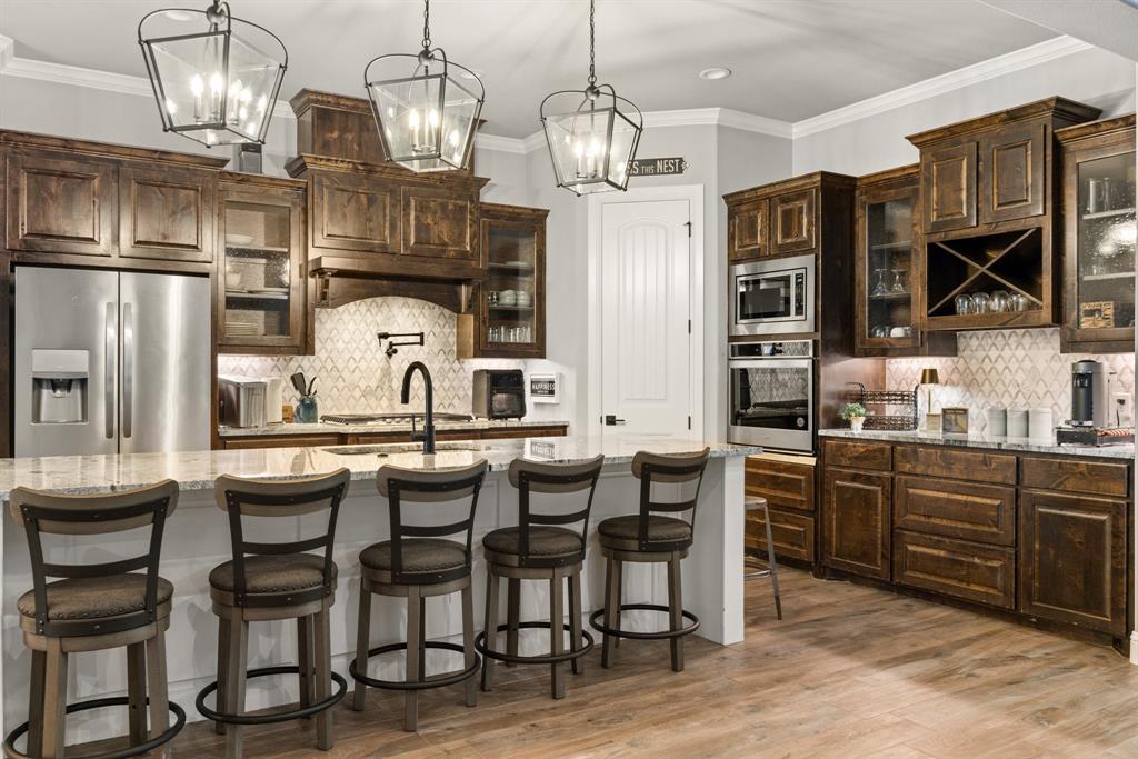 1800 Knox Road Tolar, TX 76476 - Photo 10 of 38 Spacious kitchen featuring dark wood cabinetry, stainless steel appliances, a large center island with seating, pendant lighting, and wood-finish flooring