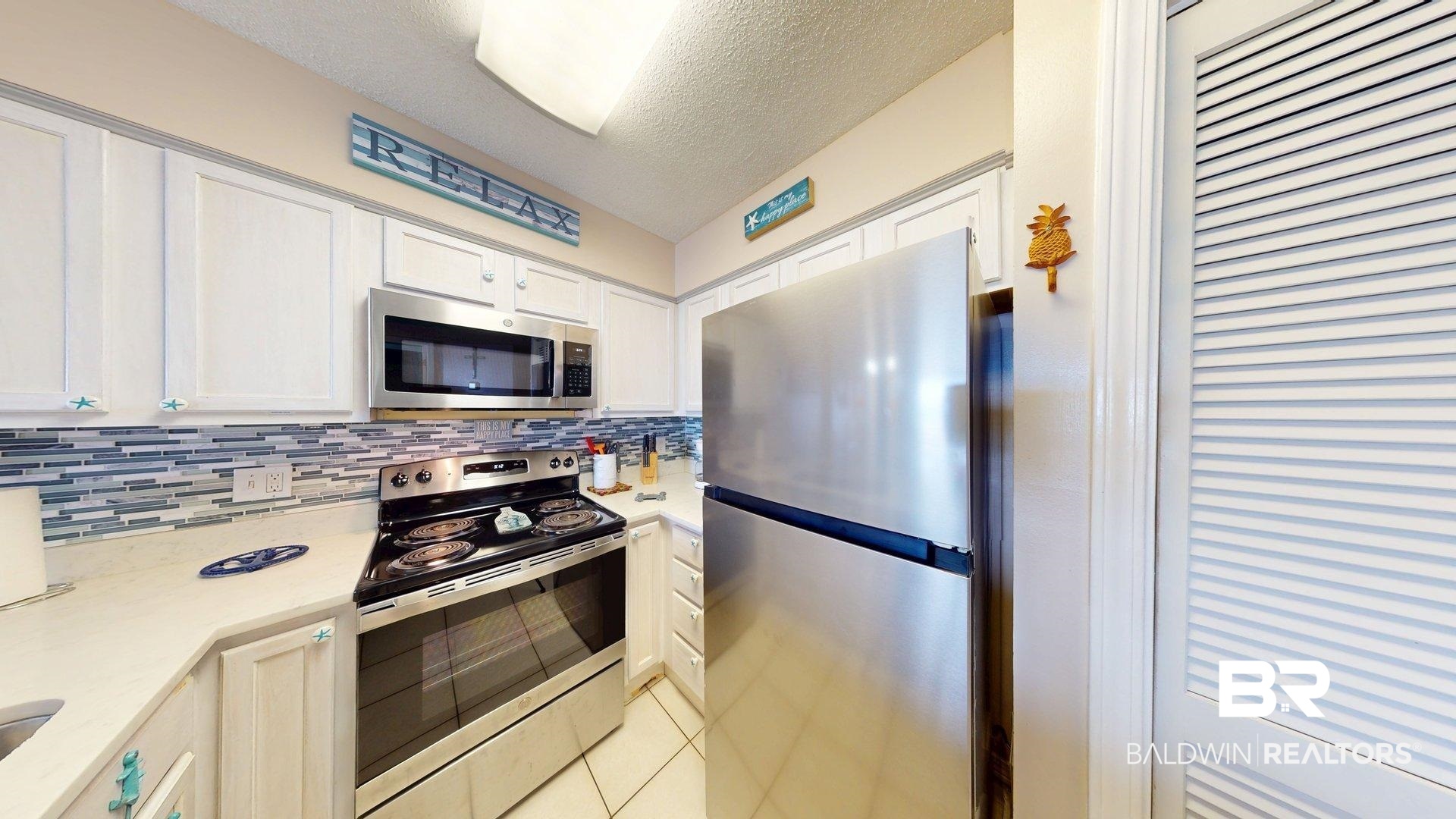645 Plantation Road, Unit 6503 Gulf Shores, AL 36542 - Photo 22 of 53 Kitchen with a textured ceiling, stainless steel appliances, light tile patterned flooring, decorative backsplash, and white cabinets