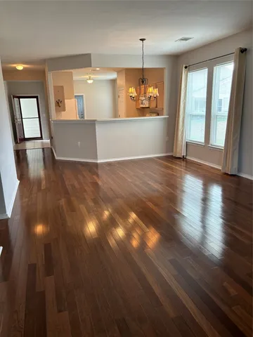 an empty room with wooden floor and kitchen view