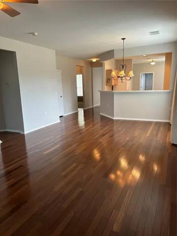an empty room with wooden floor kitchen view and a fireplace