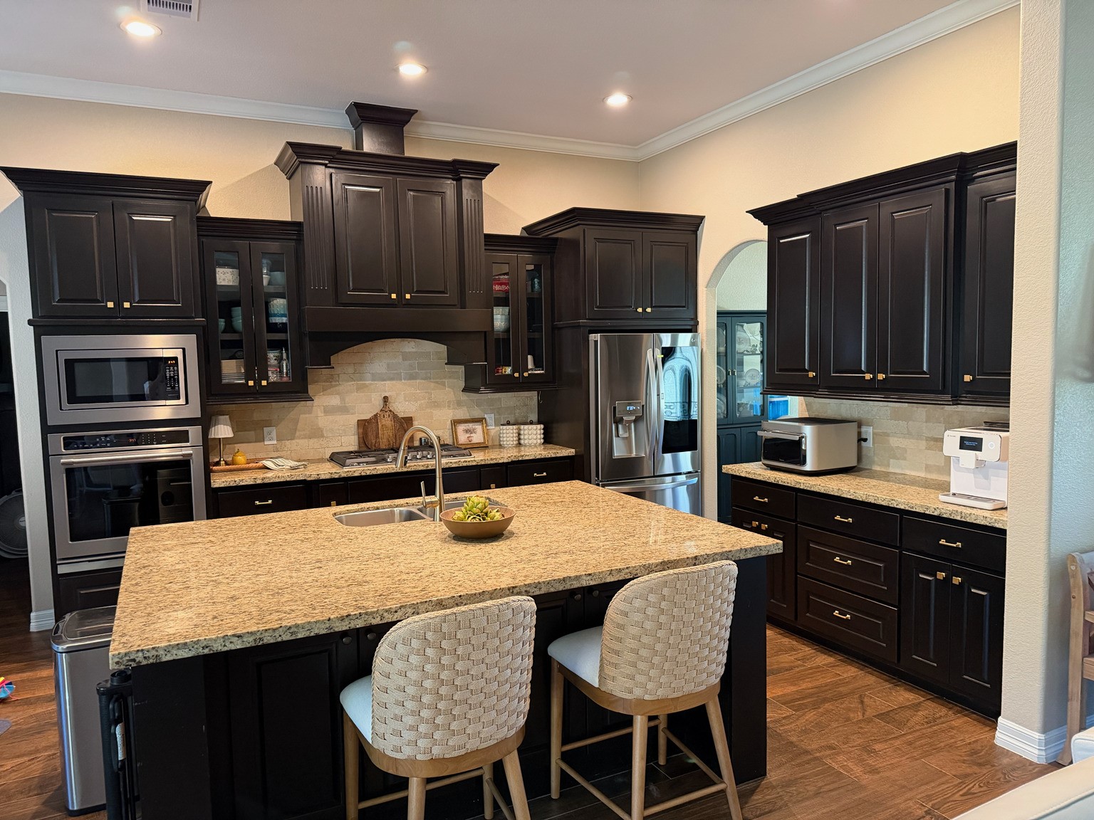 27656 Rio Blanco Drive Splendora, TX 77372 - Photo 5 of 18 This kitchen features elegant dark wood cabinets, granite countertops, and modern stainless steel appliances. It includes a central island with a sink and seating, complemented by recessed lighting and warm wood flooring for a cozy, upscale feel.