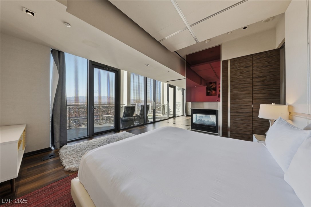 4381 West Flamingo Road, Unit 58301 Las Vegas, NV 89103 - Photo 17 of 32 Bedroom with wood finished floors, a multi sided fireplace, and a wall of windows