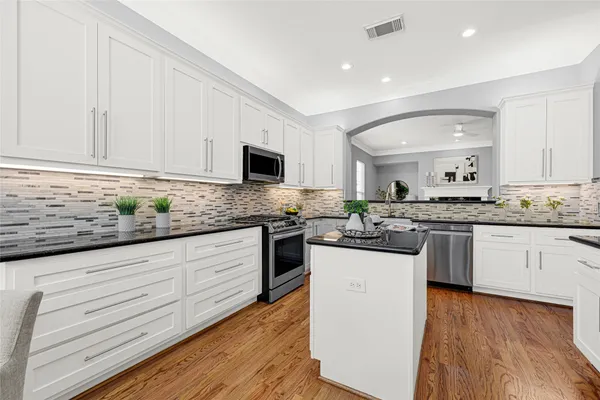 a kitchen with stainless steel appliances granite countertop a stove a sink dishwasher a refrigerator and white countertops with wooden floor