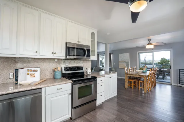 a kitchen with stainless steel appliances granite countertop a stove top oven a sink dishwasher a dining table and chairs with wooden floors