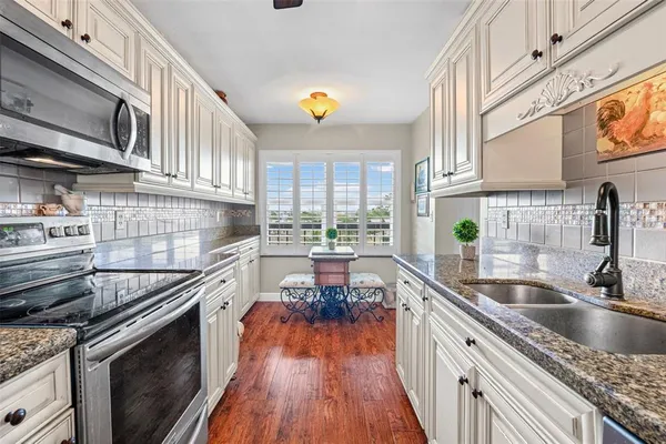 a kitchen with stainless steel appliances granite countertop a refrigerator a stove and a sink with wooden floor