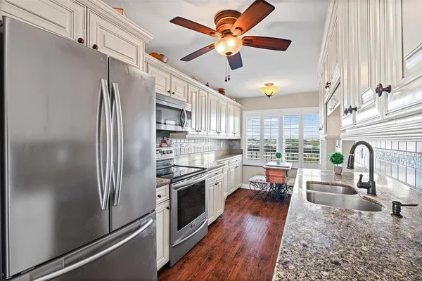 a kitchen with stainless steel appliances granite countertop a stove a sink and white cabinets with wooden floor