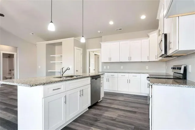 a kitchen with stainless steel appliances granite countertop a sink a stove and white cabinets with wooden floor