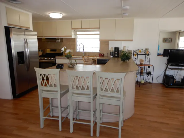 a kitchen with granite countertop a refrigerator a stove a dining table and chairs with wooden floor