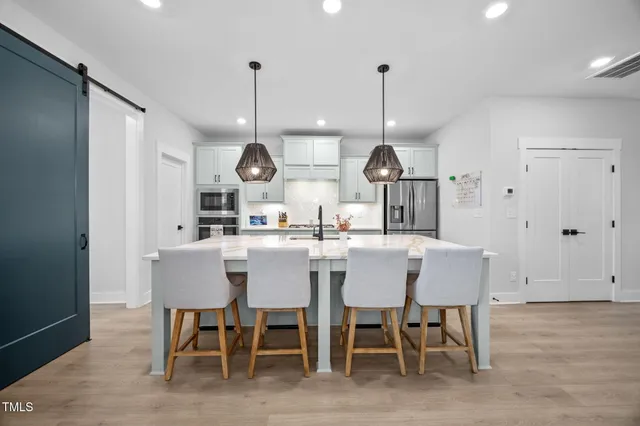 a kitchen with stainless steel appliances kitchen island granite countertop a dining table chairs and white cabinets