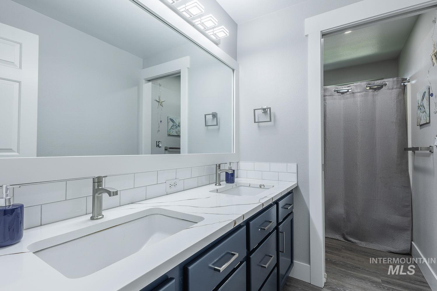 3950 Cassia Road New Plymouth, ID 83655 - Photo 20 of 26 Bathroom with a shower with curtain, double vanity, dark wood-style floors, and tasteful backsplash