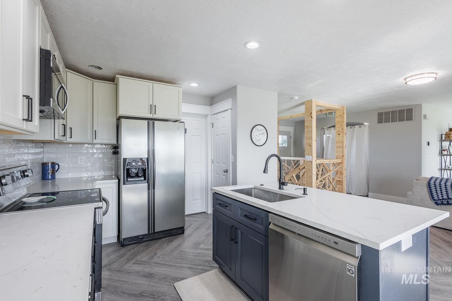 3950 Cassia Road New Plymouth, ID 83655 - Photo 6 of 26 Two tone kitchen featuring stainless steel appliances, dual tone cabinets, parquet floors, a textured ceiling, and a kitchen island with sink