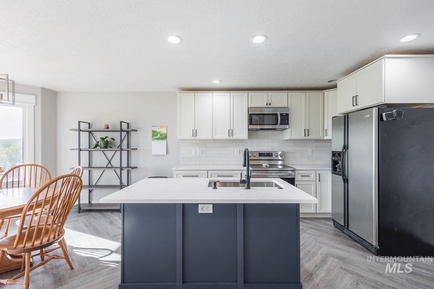 3950 Cassia Road New Plymouth, ID 83655 - Photo 7 of 26 Kitchen with stainless steel appliances, an island with sink, two tone color scheme, light stone counters, and parquet floors