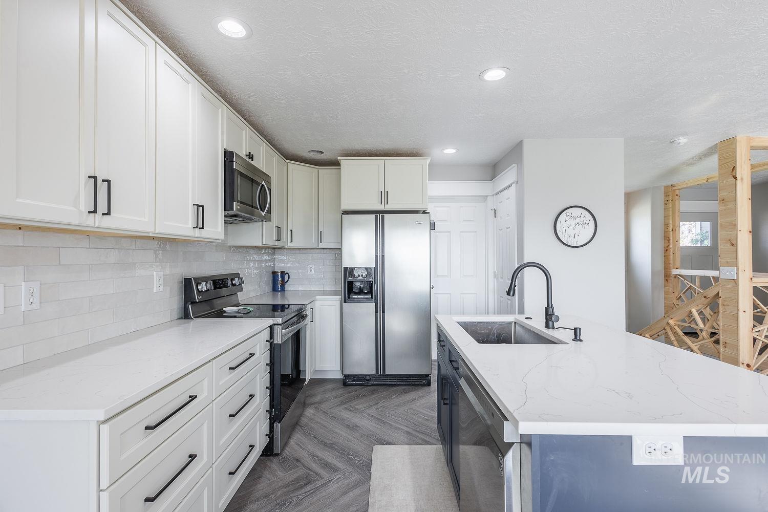 3950 Cassia Road New Plymouth, ID 83655 - Photo 8 of 26 Kitchen featuring a kitchen island with sink, stainless steel appliances, parquet floors, light stone counters, and dual tone cabinetry