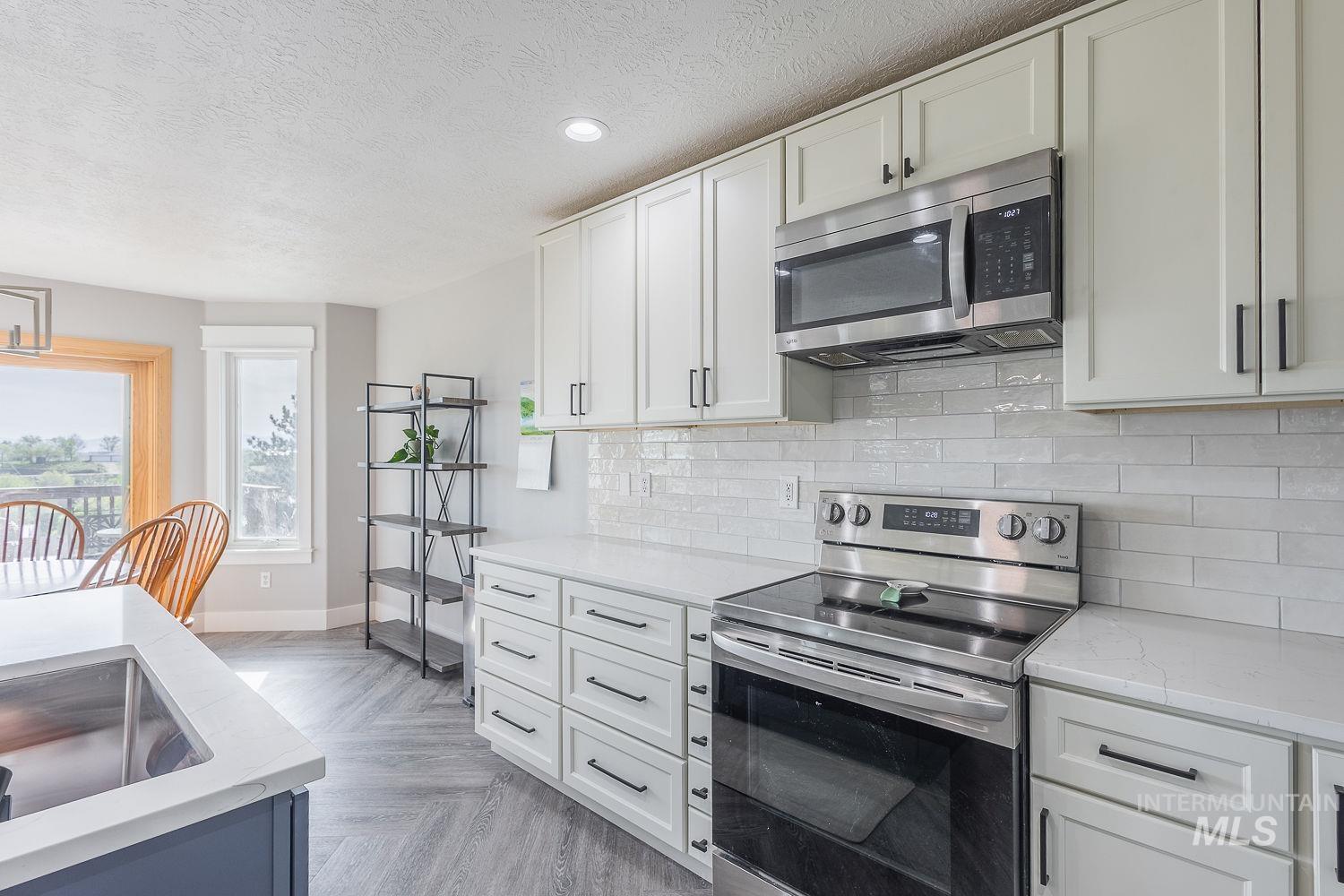 3950 Cassia Road New Plymouth, ID 83655 - Photo 9 of 26 Kitchen with stainless steel appliances, backsplash, light stone countertops, parquet floors, and a textured ceiling