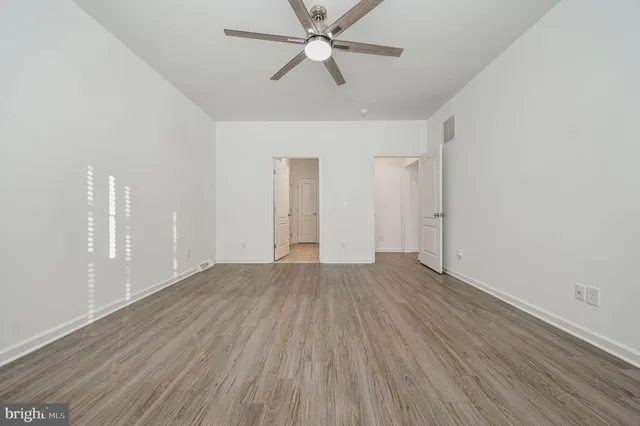 an empty room with wooden floor ceiling fan and windows