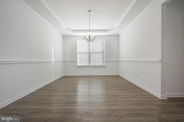 an empty room with wooden floor chandelier and windows