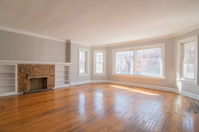 an empty room with wooden floor fireplace and windows