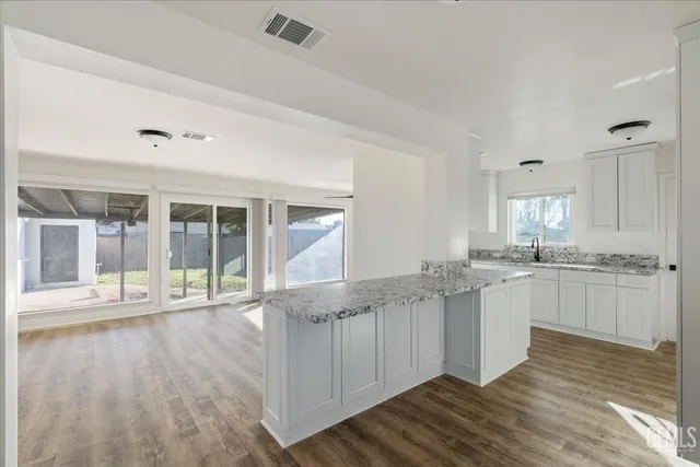 a large white kitchen with granite countertop a stove and white cabinets with wooden floor