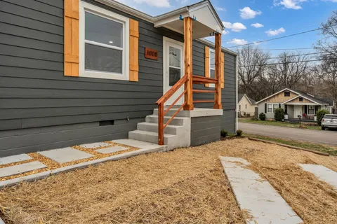 a view of house with wooden deck and a large tree