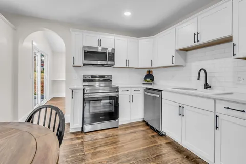 a kitchen with stainless steel appliances white cabinets a sink a stove a refrigerator and microwave with wooden floor