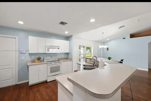 a kitchen with stainless steel appliances kitchen island granite countertop a stove a sink a refrigerator and white cabinets with wooden floor