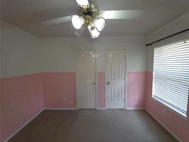 an empty room with a chandelier fan and windows