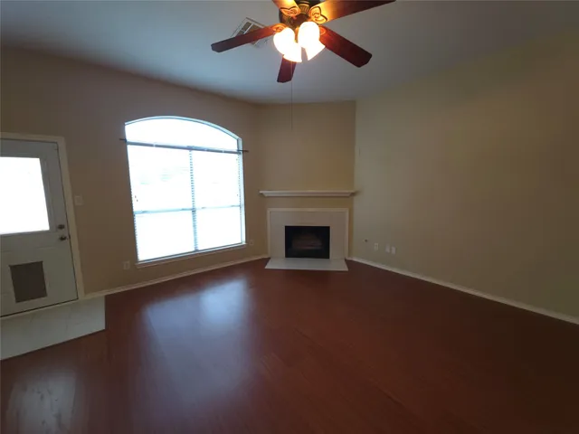 an empty room with wooden floor chandelier fan and windows