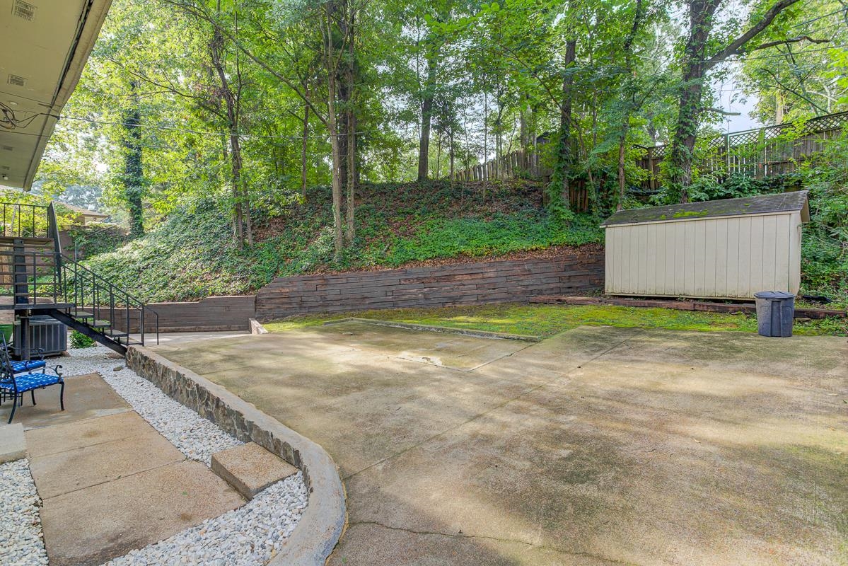 5699 Normandy Road Memphis, TN 38120 - Photo 33 of 34 Back for cars or basketball? area featuring a stone retaining wall and a white storage shed