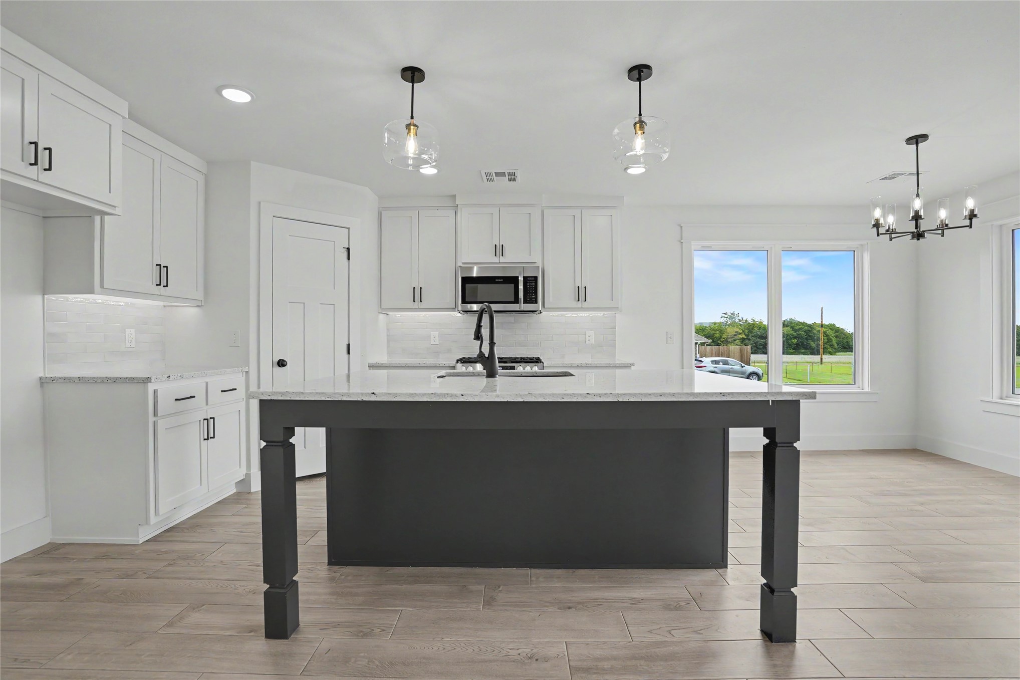 1445 South 4260th Road Chelsea, OK 74016 - Photo 10 of 33 Contemporary kitchen featuring a dark gray island with decorative legs, white cabinetry, integrated stainless steel microwave, and wood-finish flooring