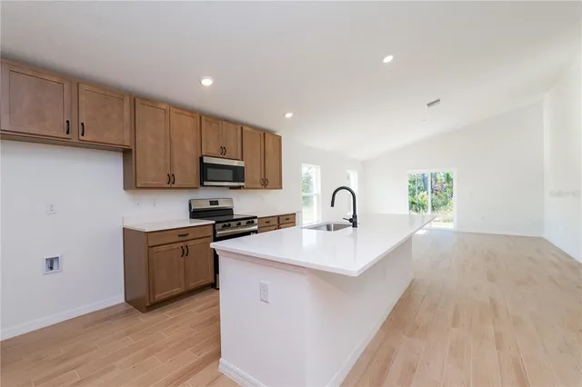 a kitchen with stainless steel appliances granite countertop a sink a stove a refrigerator cabinets and a wooden floor