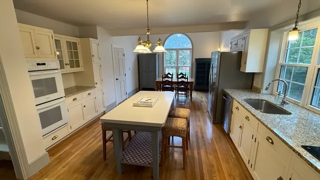 a kitchen with stainless steel appliances a stove a refrigerator a sink and white cabinets with wooden floor