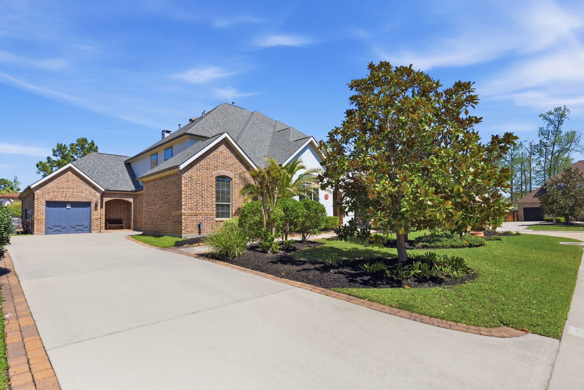 223 South Bauer Point Circle Spring, TX 77389 - Photo 4 of 50 This photo features a charming brick home with a well-maintained front yard and a spacious driveway leading to a two-car garage. The landscaping includes a large tree and manicured shrubs, enhancing the home's curb appeal. The roof is pitched with dark shingles, complementing the traditional architecture.