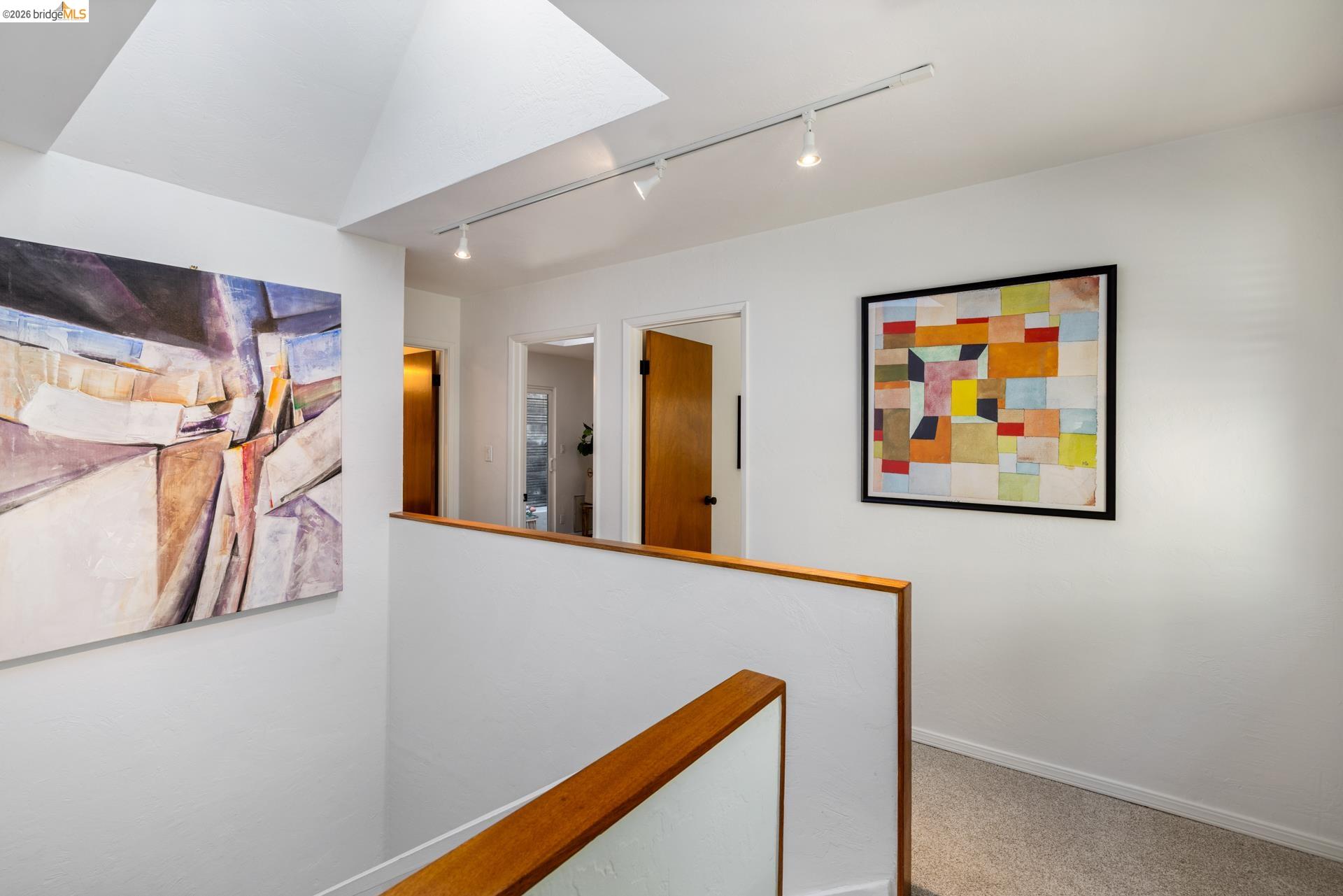 6660 Sobrante Road Oakland, CA 94611 - Photo 28 of 48 Vaulted ceiling with skylight, track lighting, light-colored carpeting, white walls, and wood-toned handrail