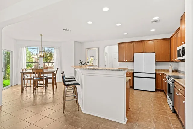 a kitchen with granite countertop a refrigerator a stove top oven and a dining table with wooden floor