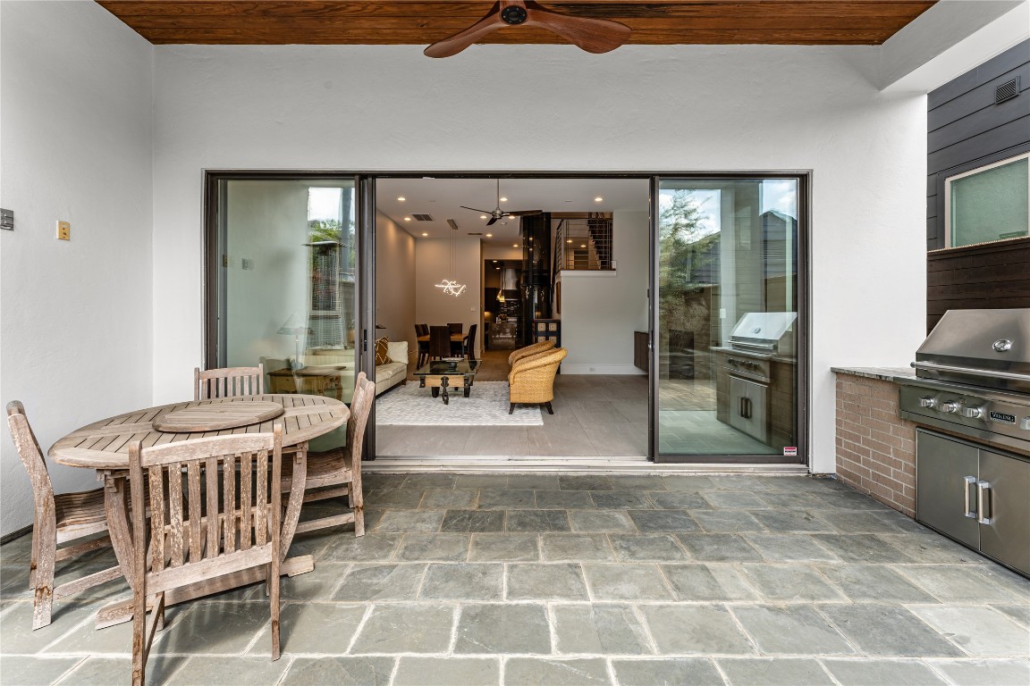 917 Peden Street Houston, TX 77006 - Photo 14 of 50 Expansive sliding glass doors create a seamless indoor-outdoor connection, opening to a covered patio with a rich wood-paneled ceiling and modern fan. This space is ideal for year-round entertaining and relaxed outdoor living. Clean architectural lines and premium finishes extend the home’s luxury aesthetic outdoors.