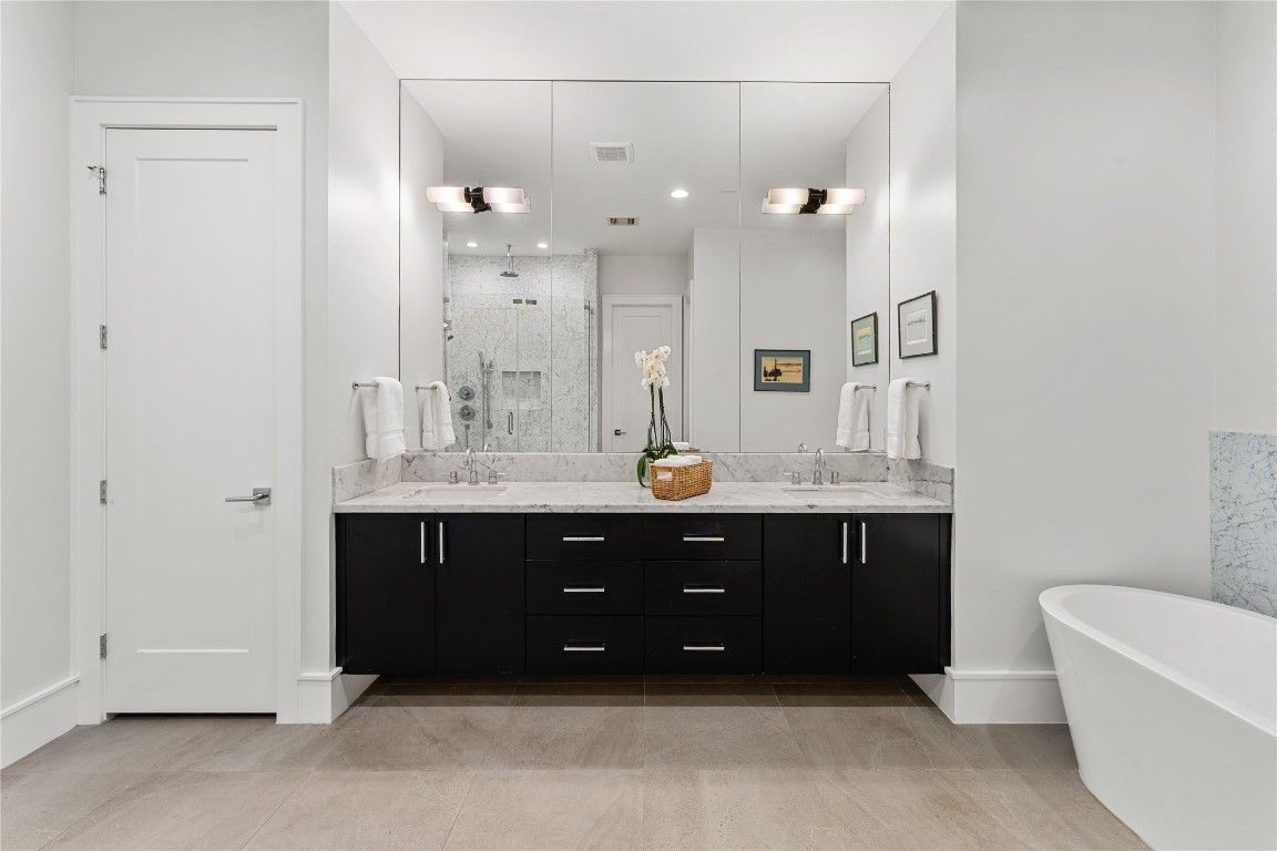 917 Peden Street Houston, TX 77006 - Photo 24 of 50 A spa-inspired primary bath featuring an expansive double vanity with marble countertops and sleek black cabinetry. Oversized mirrors and designer lighting enhance the sense of space and elegance. This thoughtfully designed layout offers both luxury and functionality.