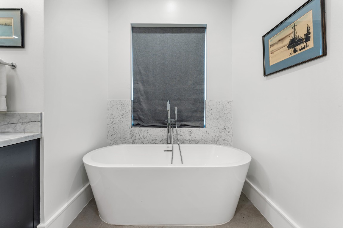 917 Peden Street Houston, TX 77006 - Photo 26 of 50 A freestanding soaking tub positioned beneath a window creates a tranquil retreat within the primary bath. Marble accents and modern fixtures elevate the space’s refined design. Perfect for unwinding in a peaceful, spa-like setting.