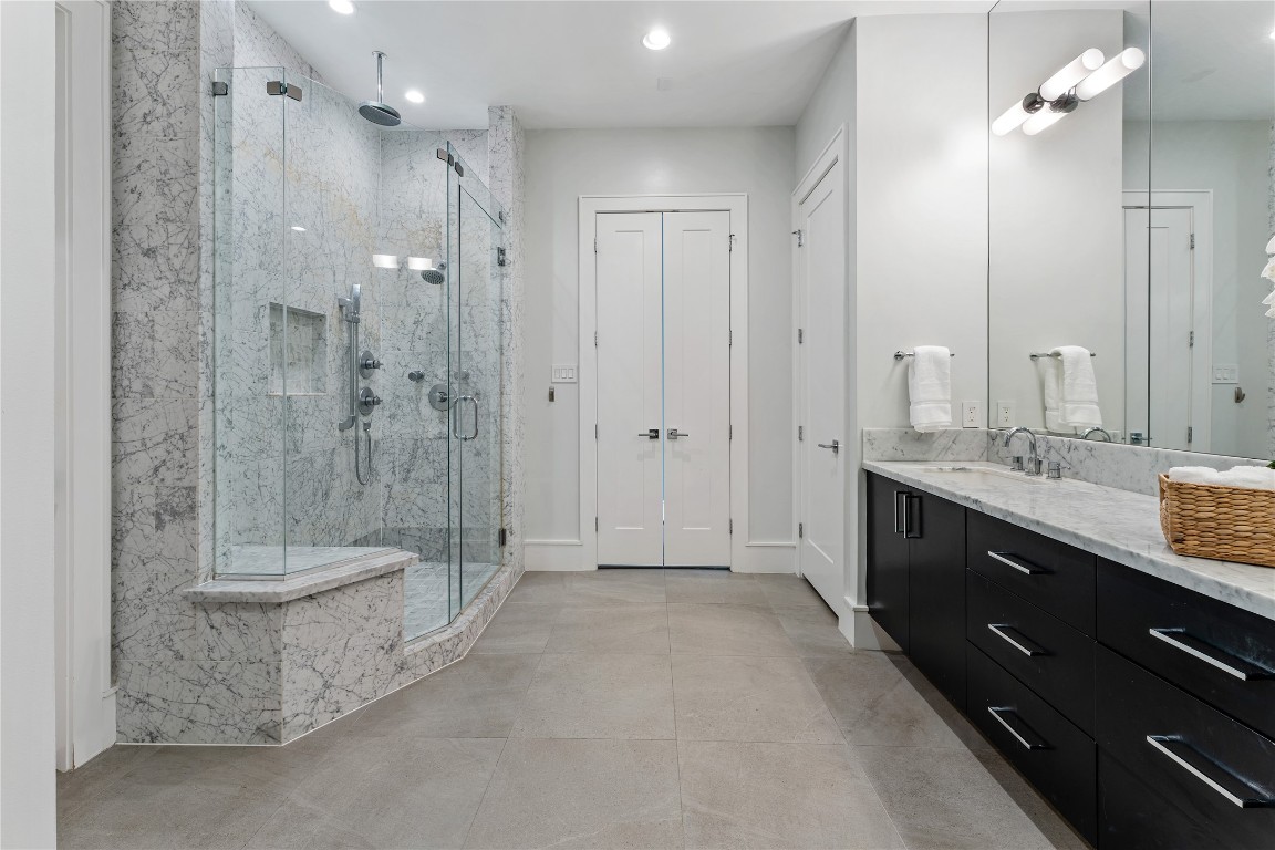 917 Peden Street Houston, TX 77006 - Photo 28 of 50 An impressive primary suite bath showcasing a marble-clad walk-in shower with frameless glass enclosure and multiple shower heads. Clean lines and high-end finishes create a serene, spa-like experience. The spacious layout is designed for ultimate comfort and relaxation.