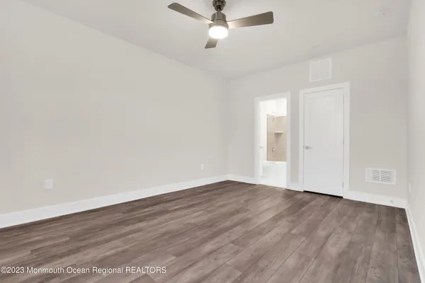 a view of an empty room with wooden floor and a ceiling fan