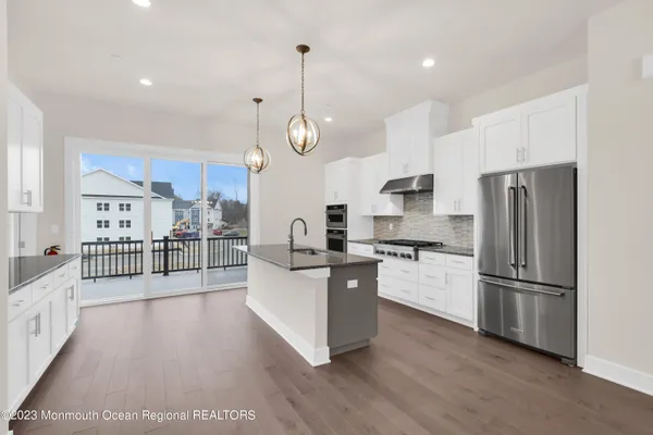 a kitchen with stainless steel appliances kitchen island granite countertop a refrigerator a stove and white cabinets with wooden floor