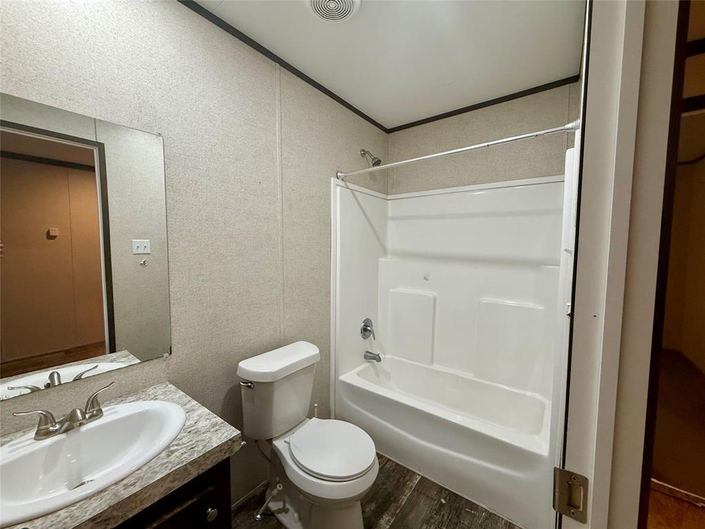 145 Adalida Lane Springtown, TX 76082 - Photo 18 of 29 Full bathroom featuring a white combination shower and tub with chrome fixtures, a single vanity with an integrated sink and wood-finish cabinetry, a commode, and wood-finish flooring