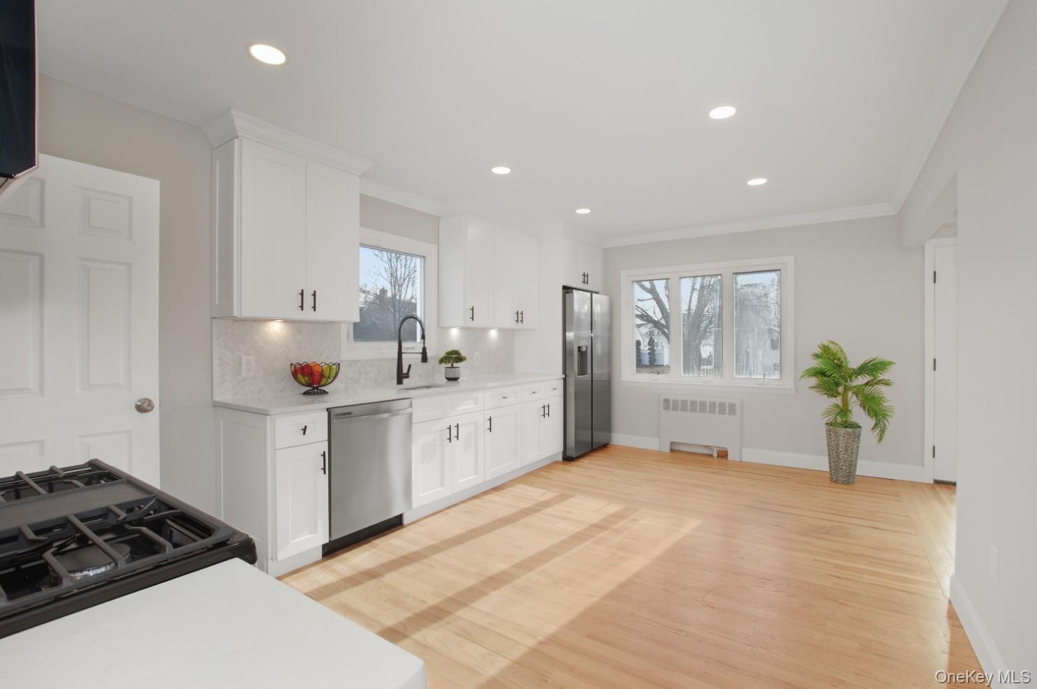 57 Remson Street Valley Stream, NY 11580 - Photo 5 of 27 Kitchen with white cabinets, light wood finished floors, radiator heating unit, stainless steel appliances, and crown molding