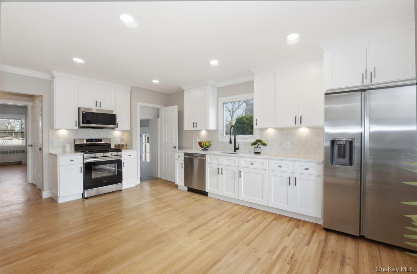 57 Remson Street Valley Stream, NY 11580 - Photo 6 of 27 Kitchen featuring stainless appliances, white shaker style cabinetry, quartz countertops, and marble backsplash