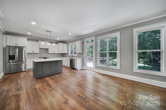 a large kitchen with stainless steel appliances granite countertop a large refrigerator a sink dishwasher a stove and white countertops with wooden floor
