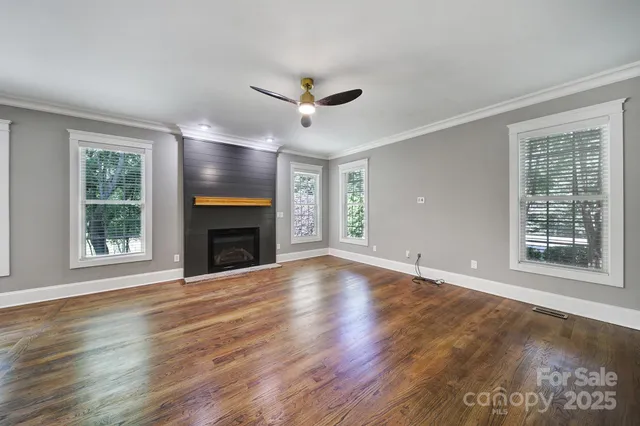 a view of an empty room with wooden floor fireplace and a window