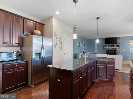 a kitchen with stainless steel appliances granite countertop a refrigerator a sink dishwasher a oven and a dining table with wooden floor